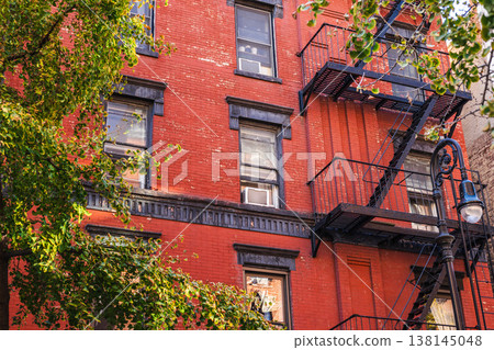 Red brick New York apartment facade with fire escape and street tree branches Red brick New York apartment facade with fire escape and street tree branches 138145048