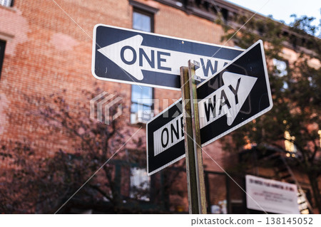 One way street signs at city intersection with urban buildings background 138145052
