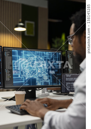 Engineer utilizing AI on computer to optimize performance and forecast issues. African american worker in tech company office training machine learning models to perform automatic updates Engineer utilizing AI on computer to optimize performance and forecast issues. African american worker in tech company office training machine learning models to perform automatic updates 138145285