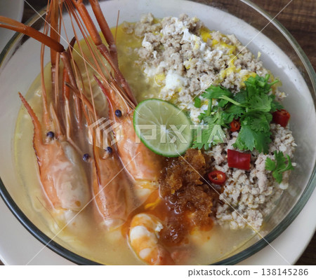 Tom Yum Kung Noodle Bowl with River Prawns, Poached Egg, Minced Pork, Lime, Chili, Herbs, and Aromatic Broth Served in a White Bowl 138145286