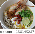 Tom Yum Kung Noodle Bowl with River Prawns, Poached Egg, Minced Pork, Lime, Chili, Herbs, and Aromatic Broth Served in a White Bowl 138145287