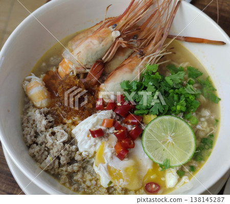 Tom Yum Kung Noodle Bowl with River Prawns, Poached Egg, Minced Pork, Lime, Chili, Herbs, and Aromatic Broth Served in a White Bowl Tom Yum Kung Noodle Bowl with River Prawns, Poached Egg, Minced Pork, Lime, Chili, Herbs, and Aromatic Broth Served in a White Bowl 138145287