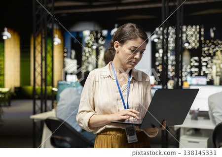 Female employee standing in office, reading emails on laptop screen, responding to inbox messages. Woman analyzing data on notebook display at night, interpreting statistical information Female employee standing in office, reading emails on laptop screen, responding to inbox messages. Woman analyzing data on notebook display at night, interpreting statistical information 138145331