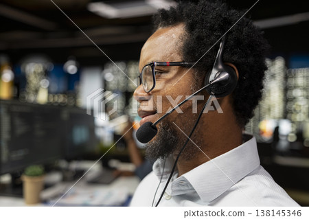Close up of startup helpdesk admin speaking in headset microphone, responding to service alerts. African american IT expert in office doing tech support, helping users across remote infrastructure Close up of startup helpdesk admin speaking in headset microphone, responding to service alerts. African american IT expert in office doing tech support, helping users across remote infrastructure 138145346