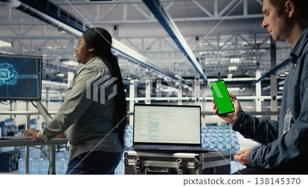 Server room software developer using mockup phone while waiting for updates to finish installing. Data center engineer uses green screen smartphone, waiting for code to finish compiling, camera A 138145370