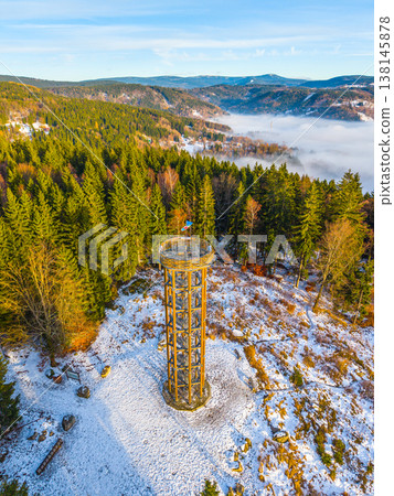 Svetly vrch lookout tower stands tall in Albrechtice, surrounded by snow-covered trees and mountains. This scene captures the winter landscape with a clear blue sky and distant hills. Svetly vrch lookout tower stands tall in Albrechtice, surrounded by snow-covered trees and mountains. This scene captures the winter landscape with a clear blue sky and distant hills. 138145878