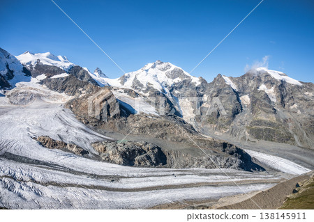 Piz Bernina rises majestically in the Swiss Alps, surrounded by rugged mountains and sprawling glaciers. The clear blue sky enhances the breathtaking landscape in Graubunden, Switzerland. 138145911
