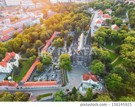Vysehrad Basilica of St. Peter and St. Paul rises majestically amid lush greenery during a golden sunrise in Prague, showcasing Gothic architecture and serene surroundings. 138145925
