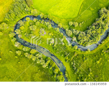 A serene river gracefully winds through a vibrant green valley in the Alps. Lush vegetation surrounds the creek, creating a picturesque landscape from a drone's perspective. 138145959