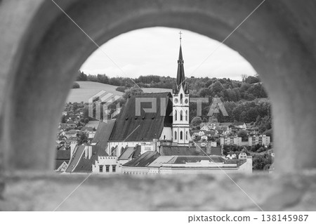 The view captures Saint Vitus Church framed by an arch. The church stands among buildings and hills in Cesky Krumlov during summer in Czechia. The view captures Saint Vitus Church framed by an arch. The church stands among buildings and hills in Cesky Krumlov during summer in Czechia. 138145987