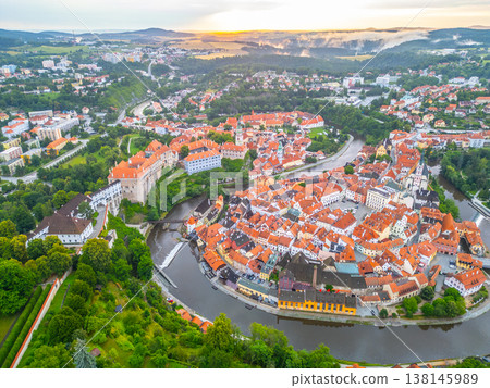 Early morning light casts a warm glow over Cesky Krumlov, highlighting the town's charming architecture and the winding Vltava River. The UNESCO site awakens in serene beauty. 138145989
