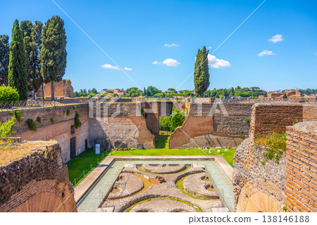 Visitors observe the Fountain of the Pelte located at the Roman Forum in Rome. The structure shows ancient stonework and historical remains under a clear blue sky. Visitors observe the Fountain of the Pelte located at the Roman Forum in Rome. The structure shows ancient stonework and historical remains under a clear blue sky. 138146188