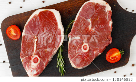 Fresh cuts of meat on a wooden board with herbs and tomatoes in a kitchen setting Fresh cuts of meat on a wooden board with herbs and tomatoes in a kitchen setting 138146853
