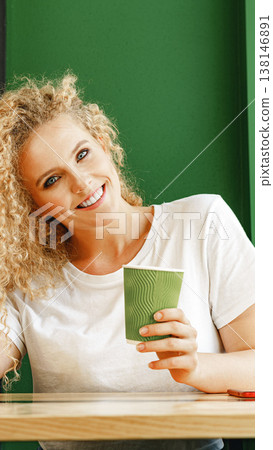 Woman smiles while holding a green cup in a cafe with green walls during daytime 138146891