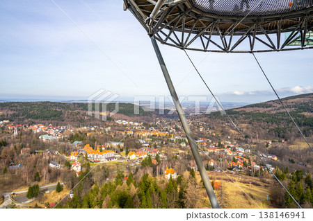 The scene shows a view from a high observation deck. Trees and hills surround a small town with colorful buildings. A clear sky can be seen in the background. The scene shows a view from a high observation deck. Trees and hills surround a small town with colorful buildings. A clear sky can be seen in the background. 138146941