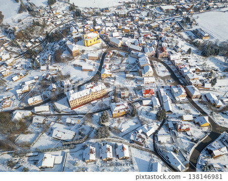 Pecka town is covered in snow during winter. This aerial view shows the layout of streets and buildings, with many rooftops blanketed in white. The scene captures the town's winter beauty. 138146981