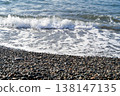 Relaxation awaits at a luxurious spa retreat by the ocean. The calming waves gently wash over smooth pebbles, creating a serene atmosphere perfect for unwinding. Blue hues enhance the tranquility. 138147135