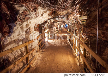 A wooden pathway stretches through a salt mine tunnel, illuminated by soft lights, showcasing intricate rock formations. This underground world creates a unique and immersive experience. 138147205