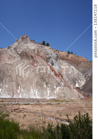 A scenic view showcases layered rock formations under a vibrant blue sky, displaying natural beauty. The landscape features earth-toned hues and distant trees. A scenic view showcases layered rock formations under a vibrant blue sky, displaying natural beauty. The landscape features earth-toned hues and distant trees. 138147219