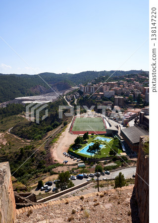 A high-angle view showcasing a picturesque cityscape with a football field, swimming pools, and lush greenery, all under a clear blue sky. 138147220