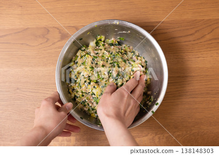 Close-up of a woman's hands mixing dumpling filling in a bowl. Close-up of a woman's hands mixing dumpling filling in a bowl. 138148303