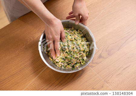 Close-up of a woman's hands mixing dumpling filling in a bowl. Close-up of a woman's hands mixing dumpling filling in a bowl. 138148304