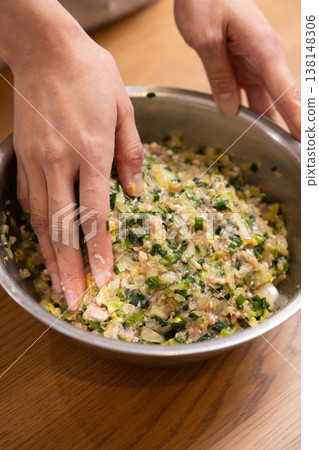 Close-up of a woman's hands mixing dumpling filling in a bowl. Close-up of a woman's hands mixing dumpling filling in a bowl. 138148306