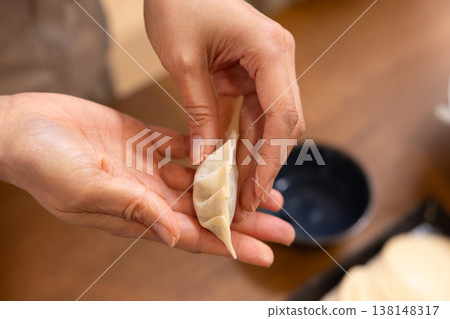 A close-up of hands wrapping the dumpling filling in the wrapper. A close-up of hands wrapping the dumpling filling in the wrapper. 138148317