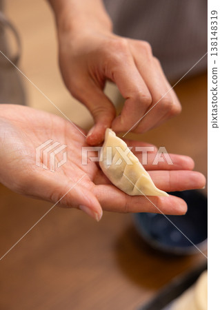 A close-up of hands wrapping the dumpling filling in the wrapper. 138148319