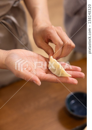 A close-up of hands wrapping the dumpling filling in the wrapper. 138148320
