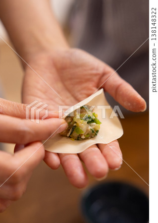 A close-up of hands wrapping the dumpling filling in the wrapper. 138148322