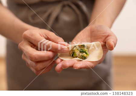A close-up of hands wrapping the dumpling filling in the wrapper. A close-up of hands wrapping the dumpling filling in the wrapper. 138148323