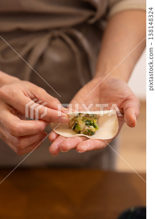 A close-up of hands wrapping the dumpling filling in the wrapper. 138148324