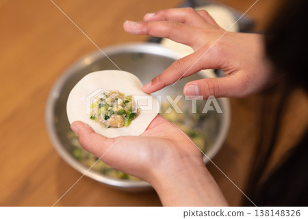 A close-up of hands wrapping the dumpling filling in the wrapper. 138148326