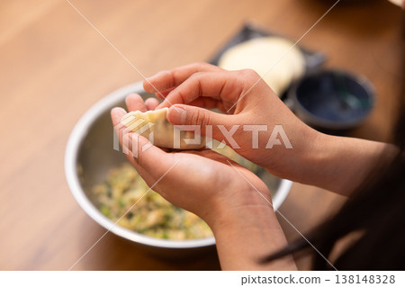 A close-up of hands wrapping the dumpling filling in the wrapper. A close-up of hands wrapping the dumpling filling in the wrapper. 138148328
