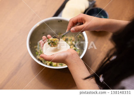 A close-up of hands wrapping the dumpling filling in the wrapper. A close-up of hands wrapping the dumpling filling in the wrapper. 138148331