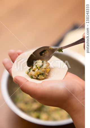 A close-up of hands wrapping the dumpling filling in the wrapper. A close-up of hands wrapping the dumpling filling in the wrapper. 138148333