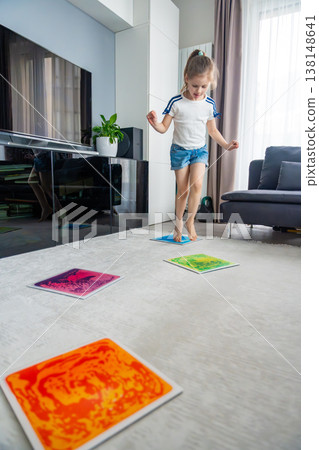 Little girl stepping and jumping on colorful sensory gel mats placed on floor at home. Sensory development, autism support and occupational therapy activity concept. Little girl stepping and jumping on colorful sensory gel mats placed on floor at home. Sensory development, autism support and occupational therapy activity concept. 138148641
