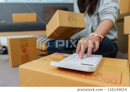 Woman calculating shipping costs for packages Woman calculating shipping costs for packages 138149654