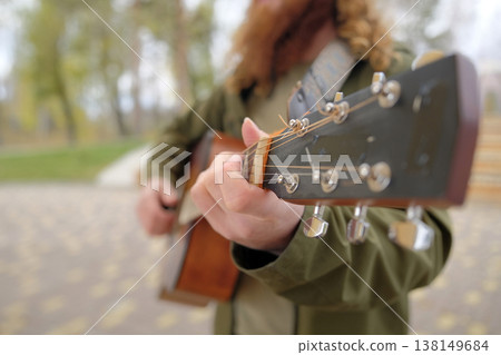 Close-up of the guitar neck, focus on the hand of a man pinching a chord. A guy with long red hair plays the guitar. The guitarist is wearing a green jacket Close-up of the guitar neck, focus on the hand of a man pinching a chord. A guy with long red hair plays the guitar. The guitarist is wearing a green jacket 138149684