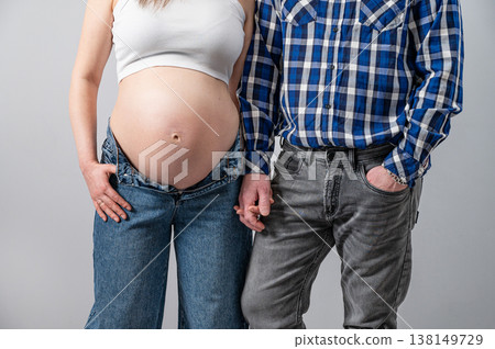 A pregnant woman in a white T-shirt and unbuttoned jeans, holding hands with her partner 138149729