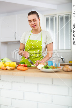 Cheerful young woman preparing vegetable salad for dinner at home Cheerful young woman preparing vegetable salad for dinner at home 138151193