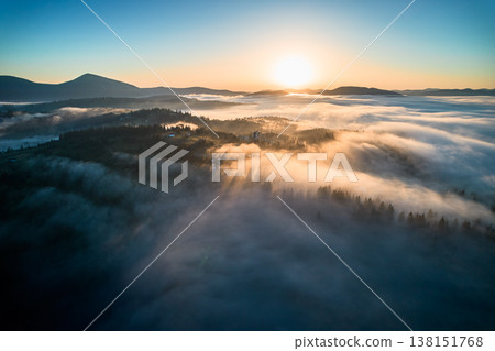 Stunning aerial view of sunrise over mountainous landscape, with thick fog blanketing valleys and hills. Sun's golden rays pierce through mist, casting serene glow over the entire scene. Stunning aerial view of sunrise over mountainous landscape, with thick fog blanketing valleys and hills. Sun's golden rays pierce through mist, casting serene glow over the entire scene. 138151768