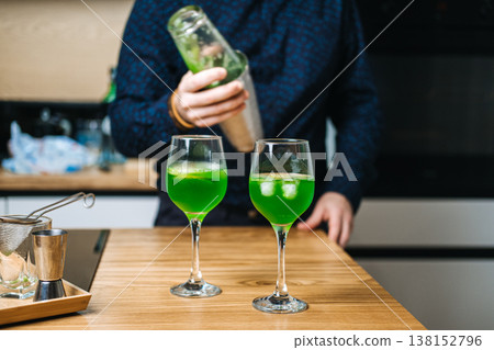 Mixing glass containing green liquid and cucumber slices sits on wooden counter next to metal shaker and lime slices. low alcohol cocktails, mindful drinking, sessionable drinks, lighter aperitifs 138152796