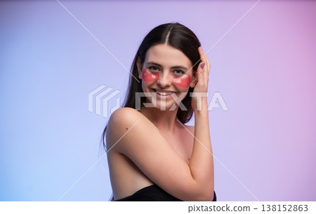 Young woman smiling while applying pink under-eye patches in a studio headshot, promoting skincare, self-care and radiant, hydrated skin with a fresh, glowing complexion Young woman smiling while applying pink under-eye patches in a studio headshot, promoting skincare, self-care and radiant, hydrated skin with a fresh, glowing complexion 138152863