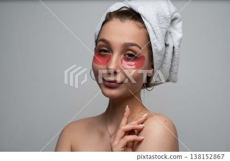 Young woman with a towel wrapped around her head applying revitalizing hydrogel eye patches, enjoying a pampering facial skincare treatment for eye bag reduction and skin wellness Young woman with a towel wrapped around her head applying revitalizing hydrogel eye patches, enjoying a pampering facial skincare treatment for eye bag reduction and skin wellness 138152867
