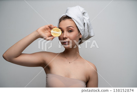Woman with a towel on her head holding a lemon half over her eye, promoting natural skincare routine, fresh vitamin C facial treatment, and healthy glowing skin Woman with a towel on her head holding a lemon half over her eye, promoting natural skincare routine, fresh vitamin C facial treatment, and healthy glowing skin 138152874