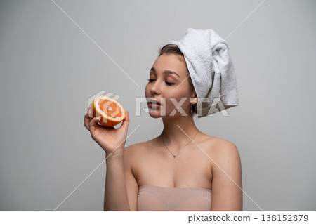 Young woman enjoying fresh natural skincare ingredients, holding grapefruit half, promoting healthy beauty routine and wellness 138152879