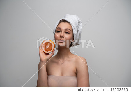 Young woman wrapped in a towel and a bandeau top holding a fresh grapefruit half near her face, embodying natural beauty, wellness, and healthy skincare concepts with fruit Young woman wrapped in a towel and a bandeau top holding a fresh grapefruit half near her face, embodying natural beauty, wellness, and healthy skincare concepts with fruit 138152883