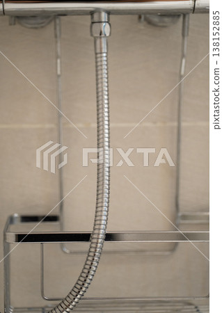 Shower hose connecting to a chrome fixture, forming part of a shower caddy and modern bathroom organization system against a tiled wall Shower hose connecting to a chrome fixture, forming part of a shower caddy and modern bathroom organization system against a tiled wall 138152885